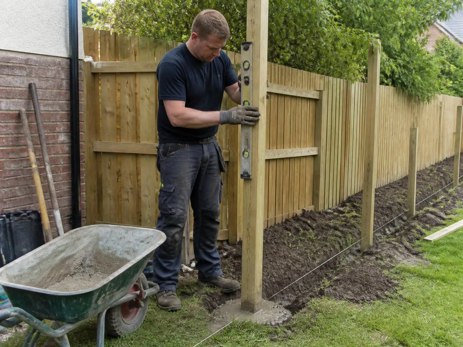 Fencing contractor levelling a timber fence post set in fresh concrete