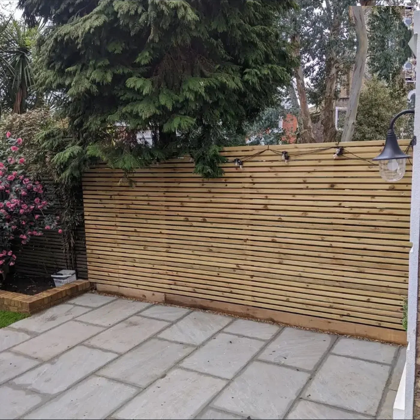 Horizontal slatted timber screen fence installed above a sandstone patio in a Beckenham garden